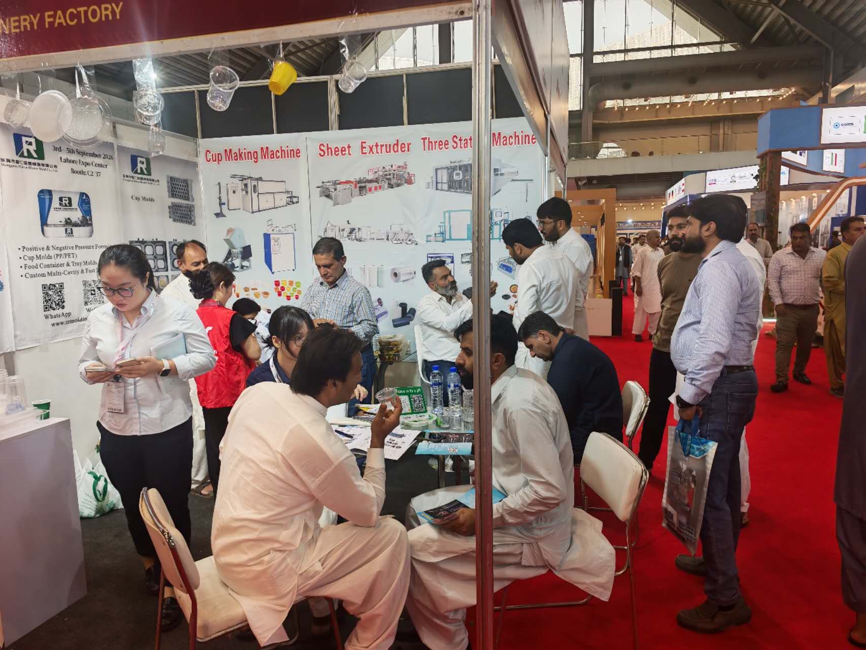 VihoX booth overview with cup making machine, sheet extruder and three station machine panels and hanging plastic cup samples, Expo Centre Lahore